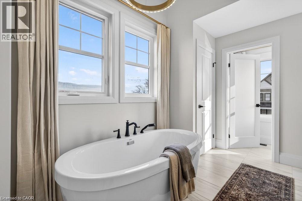 Spa-inspired primary bathroom featuring a freestanding oval soaking tub with matte black fixtures, light wood-finish flooring, and abundant natural light from multi-pane windows - 100 Watershore Drive Unit# 15, Hamilton, ON - Indoor Photo Showing Bathroom
