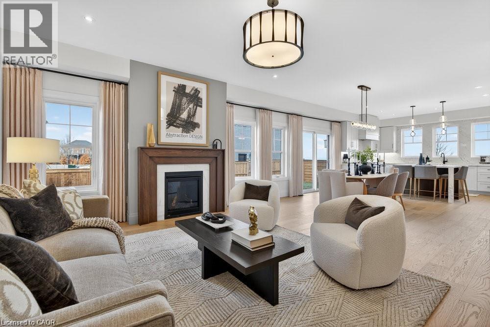Sophisticated living room featuring a wood-burning fireplace with surround mantel, curved cream-upholstered seating, geometric patterned area rug, black lacquered coffee table, and abundant natural li - 100 Watershore Drive Unit# 15, Hamilton, ON - Indoor Photo Showing Living Room With Fireplace