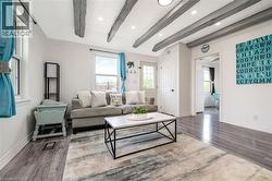 Bright and spacious living area showcasing exposed beam ceiling details, dark wood-finish flooring, and abundant natural light from large windows - 