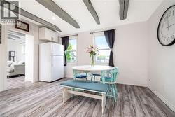 Light-filled dining area featuring wood-finish flooring, exposed ceiling beams, white walls, and a white cabinet - 