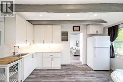 Kitchen featuring white cabinetry, gray wood-finish flooring, a stainless steel sink with a brushed nickel faucet, recessed lighting, and exposed ceiling beams - 