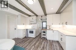 Modern kitchen featuring white cabinetry with hardware accents, stainless steel appliances including a range and microwave, quartz countertops, and wood-finish flooring - 