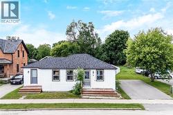 White siding exterior with dark trim windows, dark asphalt shingle roof, two wooden front steps, and a paved driveway - 