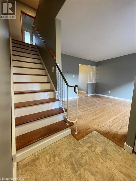 Elegant open-concept foyer showcasing a striking wood staircase with white risers and a black metal handrail, complemented by warm wood-finish flooring throughout - 683 Coronation Boulevard Unit# 2, Cambridge, ON - Indoor Photo Showing Other Room
