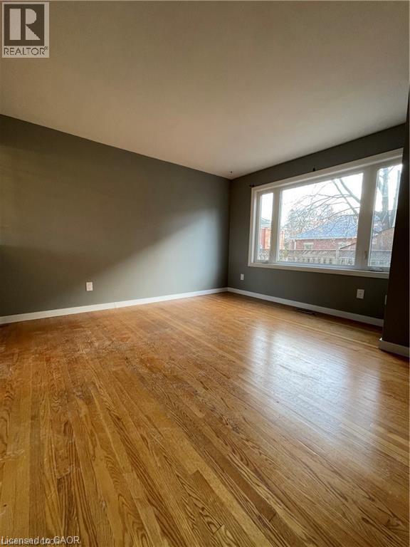 Spacious living area showcasing gleaming wood-finish flooring, neutral wall palette with accent dark wall treatment, and abundant natural light from large multi-pane windows - 683 Coronation Boulevard Unit# 2, Cambridge, ON - Indoor Photo Showing Other Room