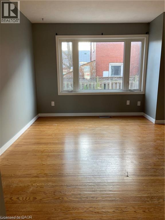 Bright corner room showcasing gleaming wood-finish flooring, neutral taupe walls, and expansive multi-pane windows framing natural light and outdoor scenery - 683 Coronation Boulevard Unit# 2, Cambridge, ON - Indoor Photo Showing Other Room