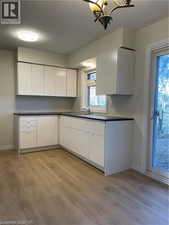 Bright, open kitchen featuring white cabinetry with ample storage, dark countertops, stainless steel appliances, recessed and pendant lighting, wood-finish flooring, and direct access to the exterior - 683 Coronation Boulevard Unit# 2, Cambridge, ON - Indoor Photo Showing Kitchen