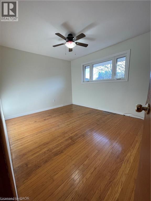 Spacious bedroom featuring rich wood-finish flooring, neutral walls, and ceiling-mounted fan with integrated lighting - 683 Coronation Boulevard Unit# 2, Cambridge, ON - Indoor Photo Showing Other Room