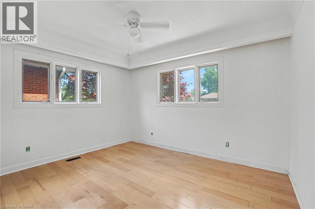 Light-filled room featuring wood-finish flooring, two large windows with white trim, a ceiling fan, and white walls - 100 Hardale Crescent, Hamilton, ON - Indoor Photo Showing Other Room