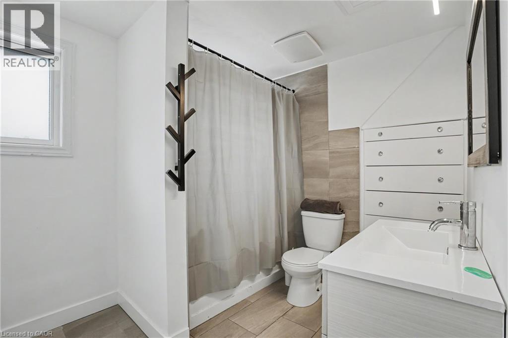 Bathroom featuring a white vanity with integrated sink, chrome faucet, tiled shower surround, recessed lighting, and a window for natural light - 100 Hardale Crescent, Hamilton, ON - Indoor Photo Showing Bathroom