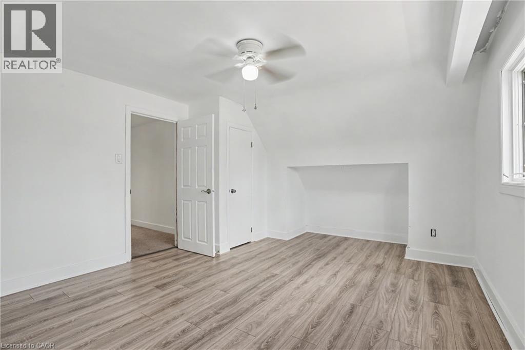 Spacious room featuring wood-finish flooring, a ceiling fan with integrated lighting, a multi-panel door, and a built-in wall niche - 100 Hardale Crescent, Hamilton, ON - Indoor Photo Showing Other Room