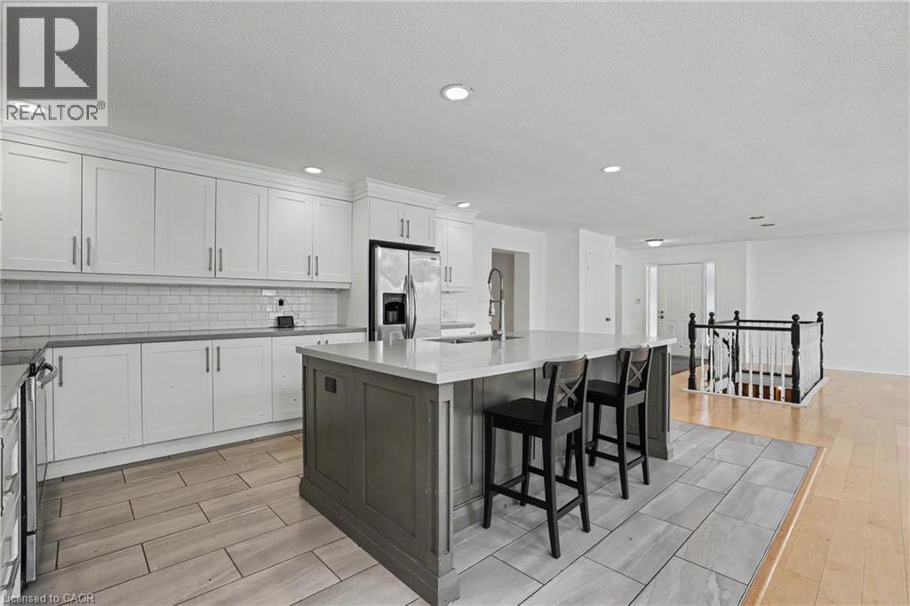 Expansive kitchen featuring a large central island with seating, white shaker cabinetry, stainless steel appliances, and a subway tile backsplash - 100 Hardale Crescent, Hamilton, ON - Indoor Photo Showing Kitchen With Upgraded Kitchen