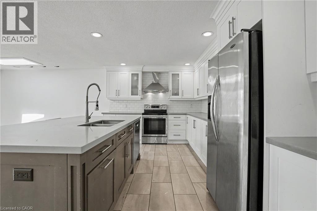 Modern kitchen featuring a large island with an undermount sink, stainless steel appliances, white shaker cabinetry, a subway tile backsplash, and light-toned tile flooring - 100 Hardale Crescent, Hamilton, ON - Indoor Photo Showing Kitchen With Double Sink With Upgraded Kitchen