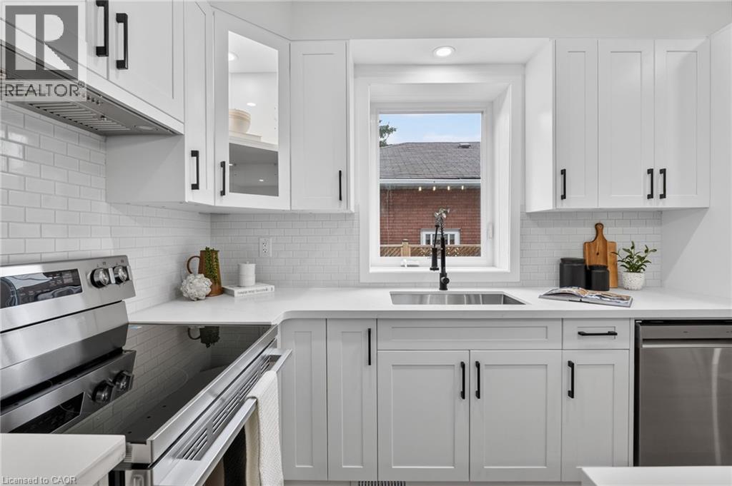 Modern kitchen featuring white shaker cabinetry with black hardware, white subway tile backsplash, stainless steel appliances, and a stainless steel sink with a matte black faucet - 325 Queensdale Avenue E, Hamilton, ON - Indoor Photo Showing Kitchen With Upgraded Kitchen
