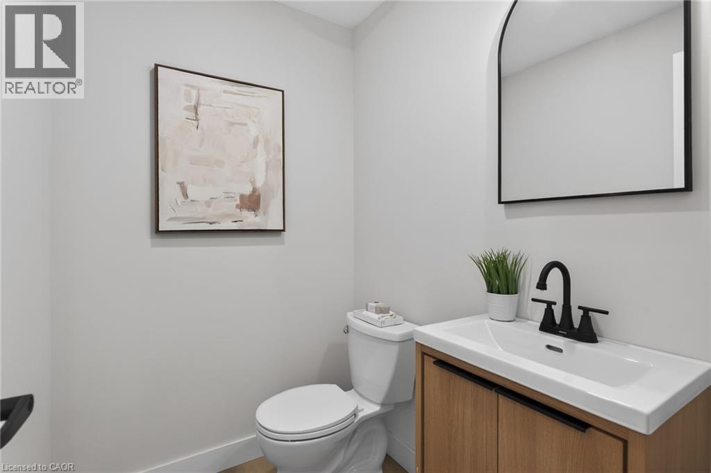 Modern powder room featuring a wood-finish vanity with an integrated white sink, matte black faucet, and an arched wall mirror - 325 Queensdale Avenue E, Hamilton, ON - Indoor Photo Showing Bathroom