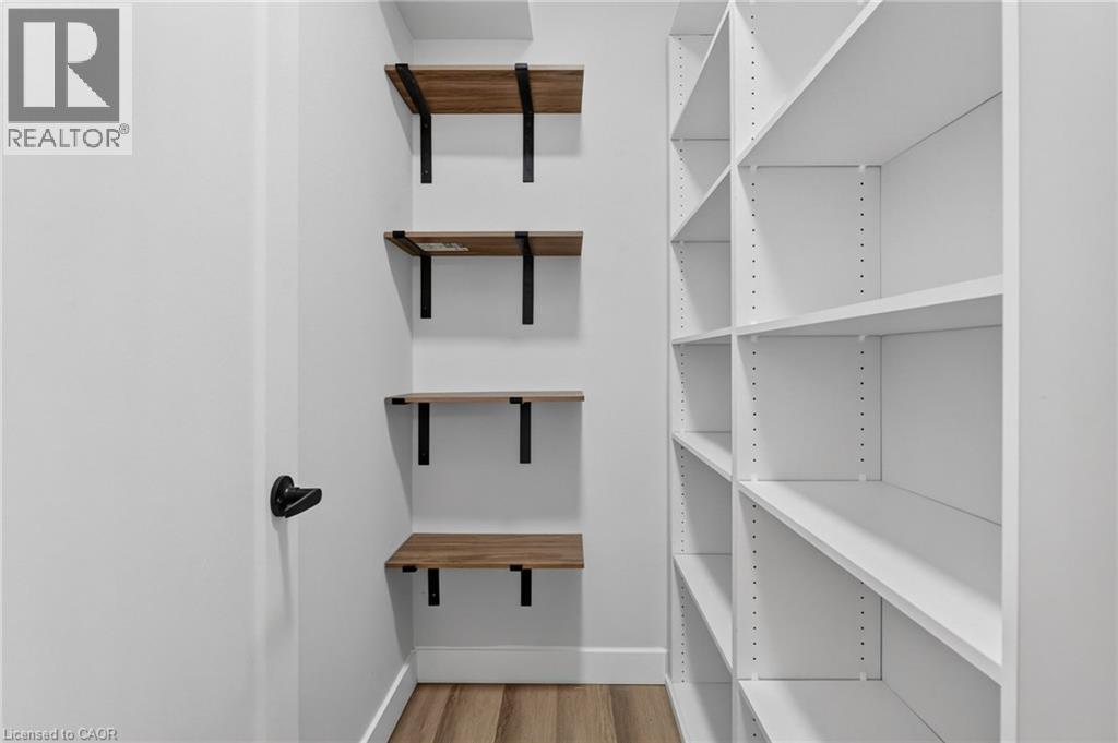 Dedicated storage area featuring white built-in shelving, wood-finish floating shelves with matte black brackets, a white door with matte black hardware, and wood-finish flooring - 325 Queensdale Avenue E, Hamilton, ON - Indoor