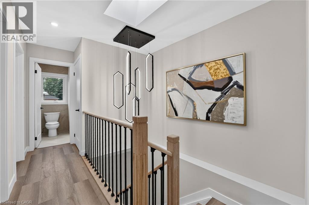 Modern hallway featuring wood-finish flooring and a contemporary linear chandelier - 325 Queensdale Avenue E, Hamilton, ON - Indoor Photo Showing Other Room