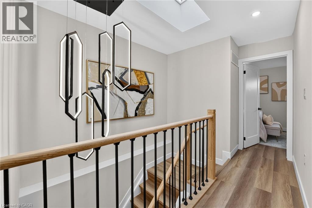 Upper-level hallway featuring a modern chandelier, wood-finish flooring, a skylight, and a staircase with a wood handrail and black metal balusters - 325 Queensdale Avenue E, Hamilton, ON - Indoor Photo Showing Other Room
