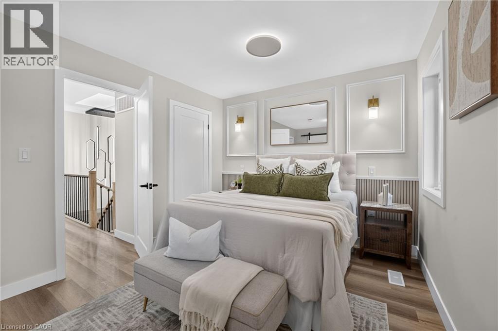 Light-filled room featuring wood-finish flooring, a contemporary ceiling light fixture, a built-in wall sconce, and a framed mirror - 325 Queensdale Avenue E, Hamilton, ON - Indoor Photo Showing Bedroom