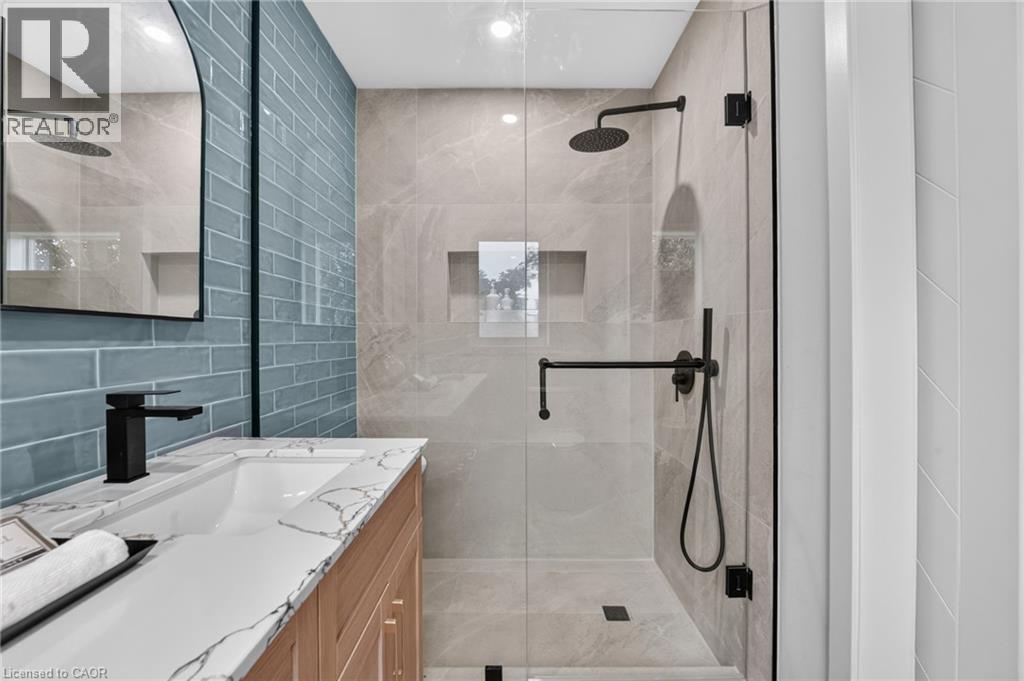 Contemporary bathroom featuring a glass-enclosed shower with matte black fixtures, a built-in shower niche, and light grey tile - 325 Queensdale Avenue E, Hamilton, ON - Indoor Photo Showing Bathroom