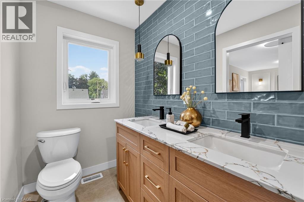 Bathroom featuring a dual vanity with wood-finish cabinetry, white countertops with veining, and matte black fixtures - 325 Queensdale Avenue E, Hamilton, ON - Indoor Photo Showing Bathroom