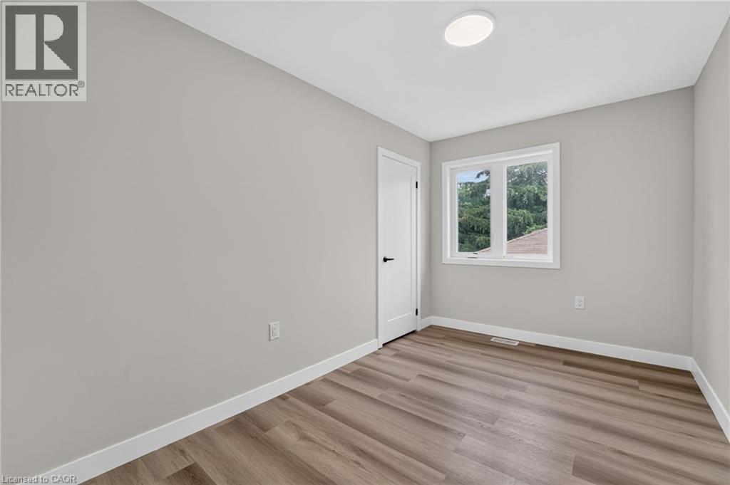 Interior room featuring light gray walls, wood-finish flooring, white baseboards, a white interior door with black hardware, and a white-framed window - 325 Queensdale Avenue E, Hamilton, ON - Indoor Photo Showing Other Room