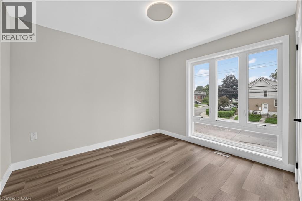 Bright room featuring a large, multi-pane window with white trim, wood-finish flooring, light gray walls, and white baseboards - 325 Queensdale Avenue E, Hamilton, ON - Indoor Photo Showing Other Room