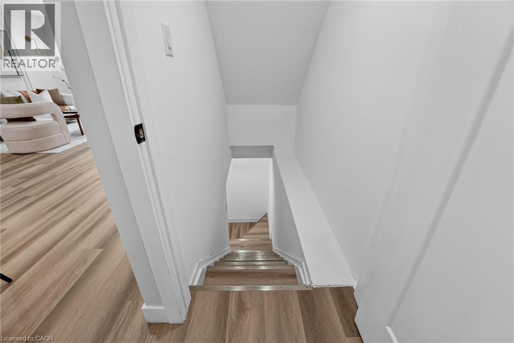 Stairwell featuring wood-finish flooring with metallic stair nosing, white baseboards, and bright white walls - 325 Queensdale Avenue E, Hamilton, ON - Indoor Photo Showing Other Room