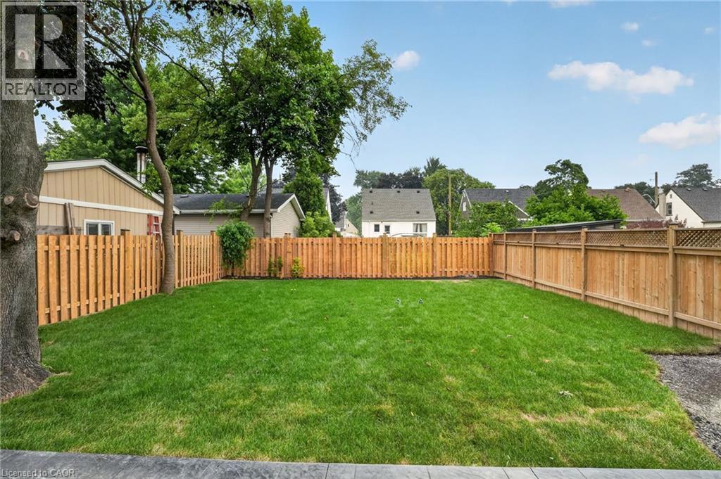 Expansive backyard featuring a lush green lawn, full privacy fencing, mature trees, and a concrete perimeter - 325 Queensdale Avenue E, Hamilton, ON - Outdoor With Backyard