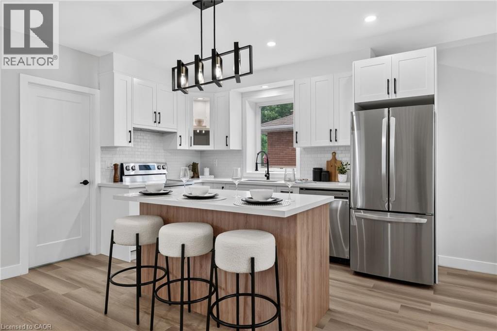 Modern kitchen featuring white shaker cabinetry, stainless steel appliances, a center island with seating, a subway tile backsplash, and wood-finish flooring - 325 Queensdale Avenue E, Hamilton, ON - Indoor Photo Showing Kitchen With Upgraded Kitchen