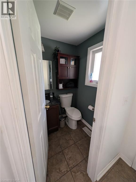 Compact half bath featuring a two-piece toilet, pedestal sink, dark tile flooring, and rich burgundy cabinetry with upper shelving - 466 Bankside Drive, Kitchener, ON - Indoor Photo Showing Bathroom