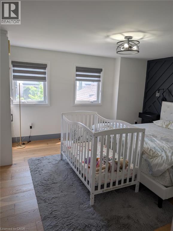 Bright secondary bedroom featuring hardwood flooring, two large double-hung windows with cellular shades providing natural light, and a ceiling-mounted fixture - 466 Bankside Drive, Kitchener, ON - Indoor Photo Showing Bedroom