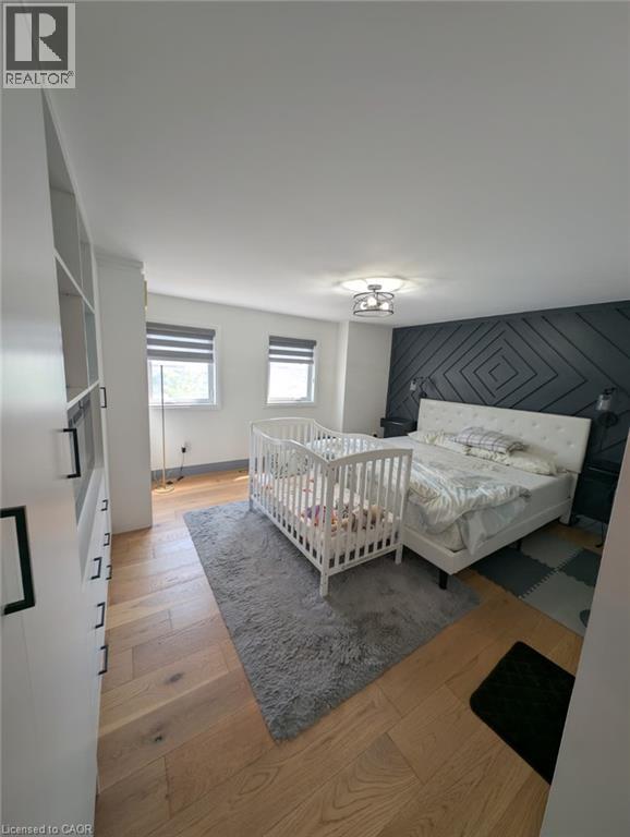 Spacious primary bedroom suite featuring hardwood flooring, dual windows with natural light, a geometric accent wall with modern paneling, ceiling-mounted lighting fixture, and an adjoining nursery sp - 466 Bankside Drive, Kitchener, ON - Indoor Photo Showing Bedroom