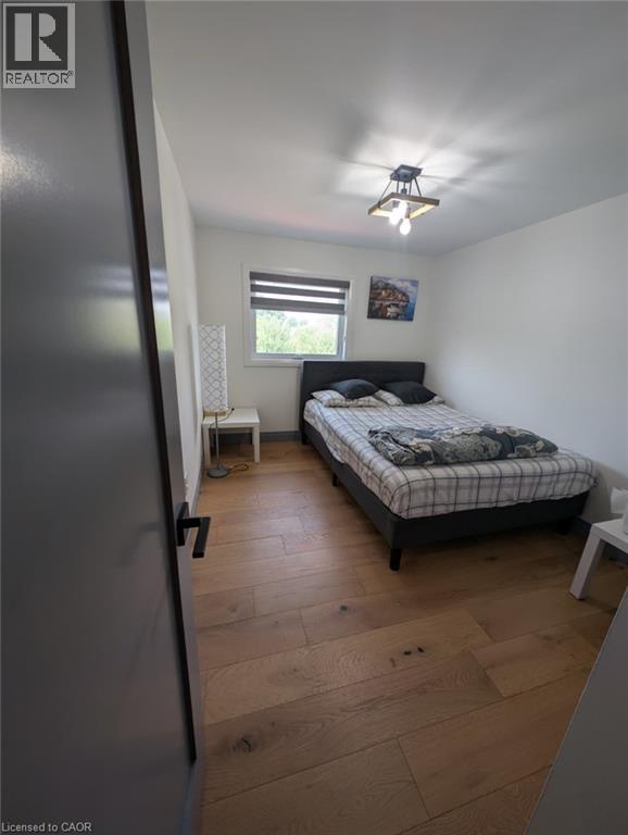 Bedroom featuring wood-finish flooring, a black platform bed frame, striped window treatment with natural light, ceiling-mounted light fixture, and convenient bedside surface - 466 Bankside Drive, Kitchener, ON - Indoor Photo Showing Bedroom