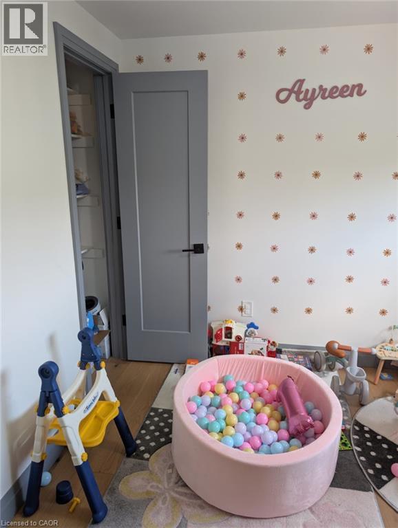 Light-toned walls with decorative accents, a modern gray panel door with matte black hardware, and wood-finish flooring - 466 Bankside Drive, Kitchener, ON - Indoor Photo Showing Other Room