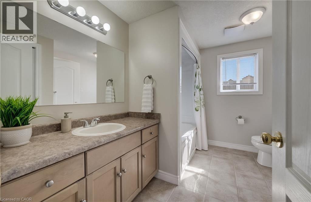 Bathroom featuring a vanity with an integrated sink, a large mirror, a four-light fixture, a built-in bathtub with shower, and tile flooring - 496 Langlaw Drive, Cambridge, ON - Indoor Photo Showing Bathroom