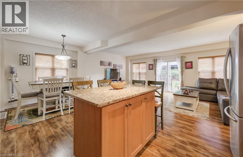 Open-concept living space featuring wood-finish flooring, a kitchen island with stone-finish countertop, and a dining area with pendant lighting - 521 Snowdrop Court, Kitchener, ON - Indoor