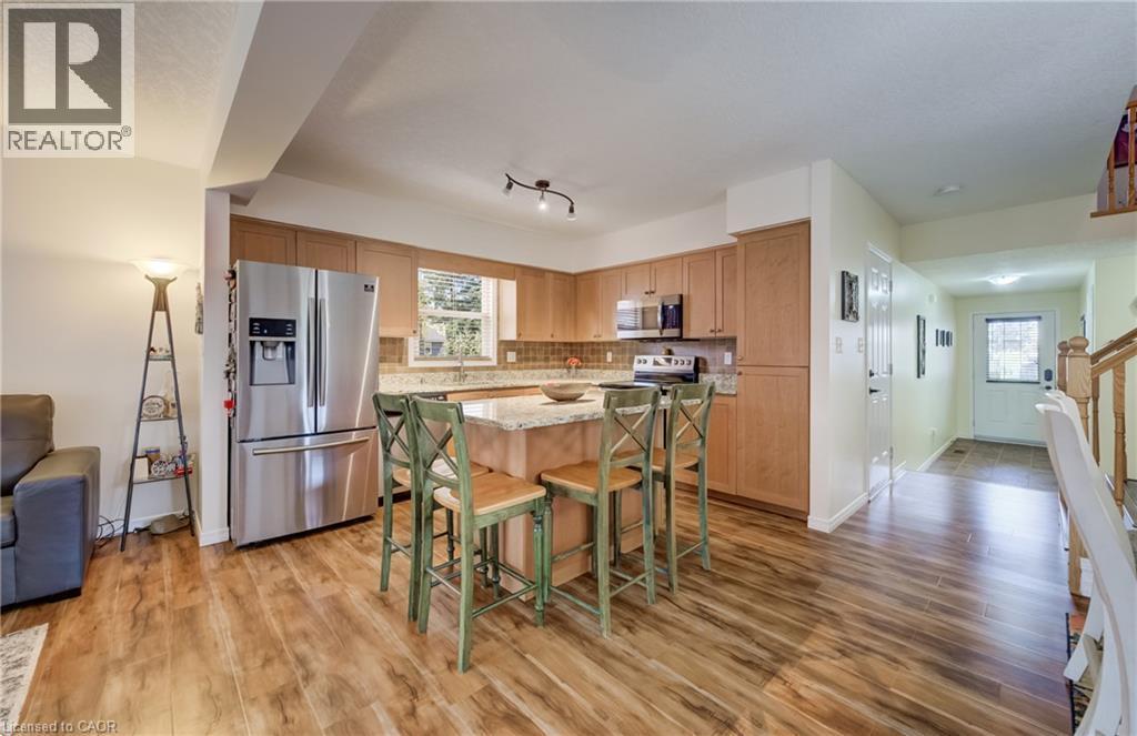 Kitchen featuring wood-finish flooring, light wood cabinetry, a center island with a light stone countertop, stainless steel appliances, and a tiled backsplash - 521 Snowdrop Court, Kitchener, ON - Indoor