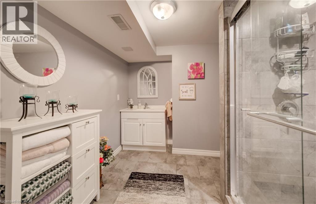 Bathroom featuring a white vanity with an integrated sink, a glass-enclosed shower with tiled walls, and stone-look tile flooring - 521 Snowdrop Court, Kitchener, ON - Indoor Photo Showing Bathroom