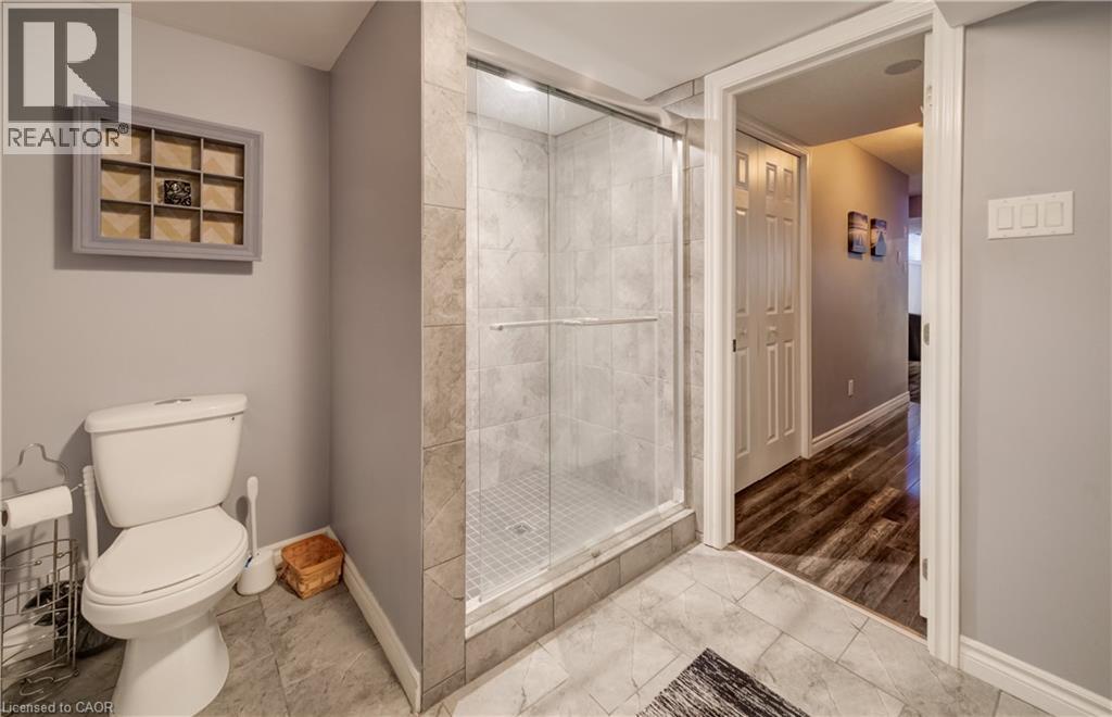 Three-piece bathroom featuring a glass-enclosed shower with tiled walls, a standard toilet, and large format tiled flooring - 521 Snowdrop Court, Kitchener, ON - Indoor Photo Showing Bathroom