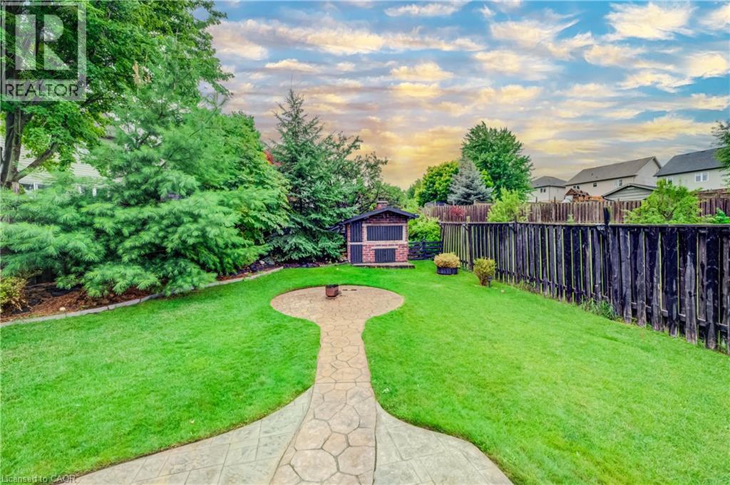 Expansive backyard featuring a stone-stamped concrete pathway, manicured lawn, mature trees, and a brick and wood-finish outdoor structure - 521 Snowdrop Court, Kitchener, ON - Outdoor