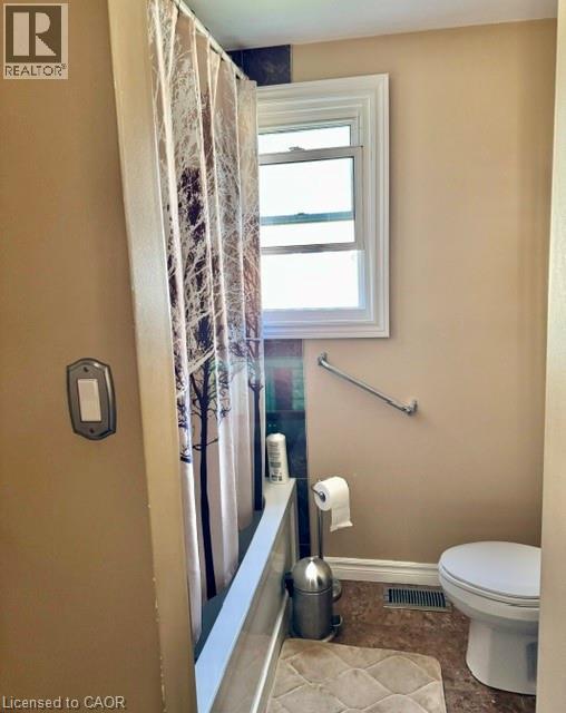 Bathroom featuring a white bathtub, a window with white trim, a toilet, a chrome grab bar, and a floor register - 342 Barton Street, Hamilton, ON - Indoor Photo Showing Bathroom
