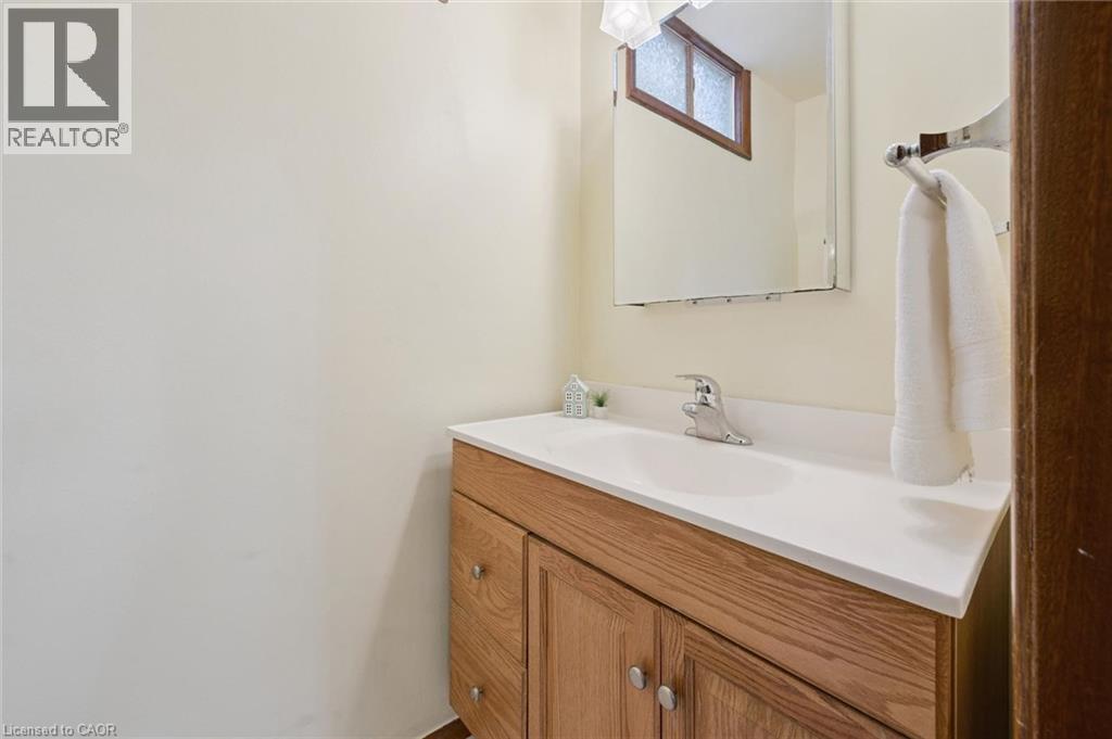 Bathroom vanity featuring a light wood-finish cabinet with silver hardware, an integrated white sink, a chrome faucet, and a wall-mounted mirror - 18 Strathcona Crescent, Kitchener, ON - Indoor Photo Showing Bathroom