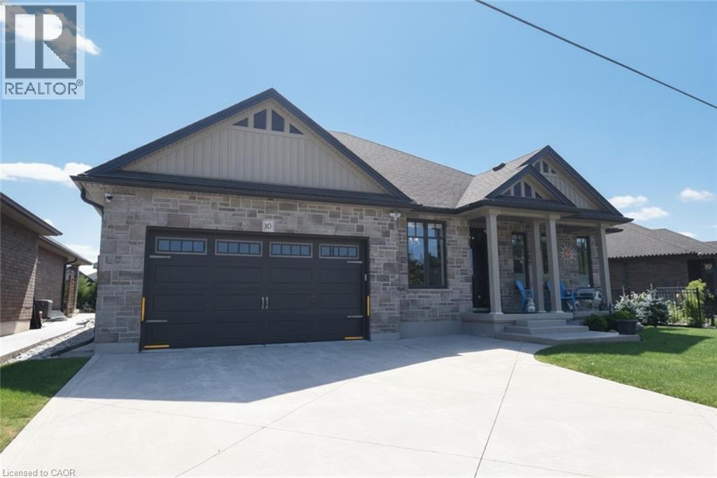 Stone facade home featuring a prominent two-car garage with transom windows, a covered front porch with pillars, and a concrete driveway - 10 Craddock Boulevard, Jarvis, ON - Outdoor