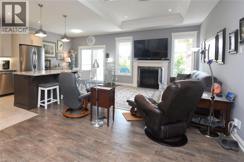 Open-concept living space showcasing wood-finish flooring throughout, a kitchen island with pendant lighting, stainless steel appliances, and a fireplace with built-in cabinetry - 10 Craddock Boulevard, Jarvis, ON - Indoor With Fireplace
