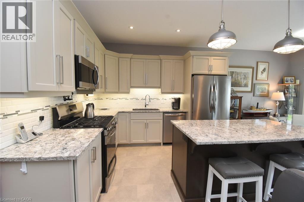 Chef's kitchen featuring cream-finish cabinetry, granite-style countertops, stainless steel appliances including a gas cooktop and built-in microwave, pendant lighting, and a large island with seating - 10 Craddock Boulevard, Jarvis, ON - Indoor Photo Showing Kitchen With Upgraded Kitchen