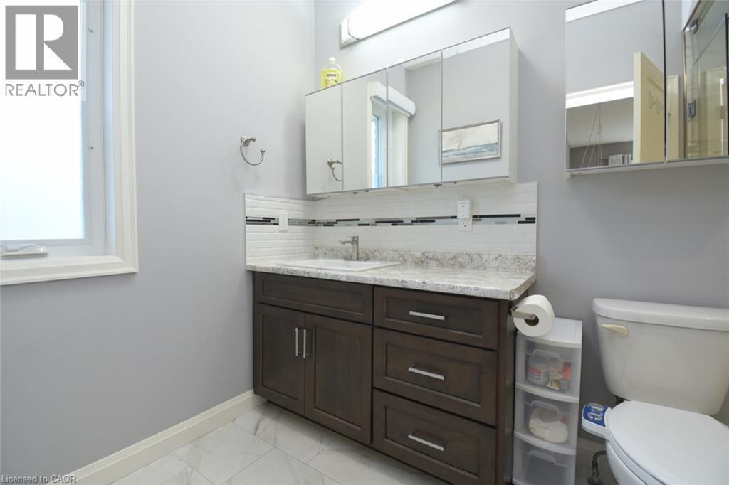Modern bathroom featuring a dark wood vanity with dual sinks, white quartz countertop with integrated backsplash, and polished chrome fixtures - 10 Craddock Boulevard, Jarvis, ON - Indoor Photo Showing Bathroom