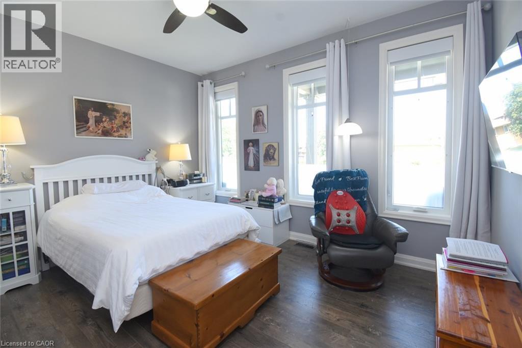 Bright, light-filled bedroom featuring a white wooden bed frame, hardwood flooring, and multiple large windows with sheer curtains - 10 Craddock Boulevard, Jarvis, ON - Indoor Photo Showing Bedroom
