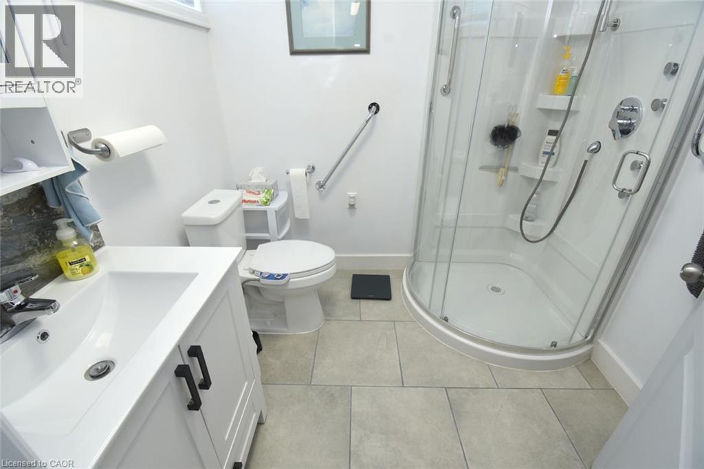 Modern bathroom featuring a clean-lined vanity with integrated sink, ceramic tile flooring, and a corner walk-in shower enclosure with multiple showerheads and grab bars - 10 Craddock Boulevard, Jarvis, ON - Indoor Photo Showing Bathroom