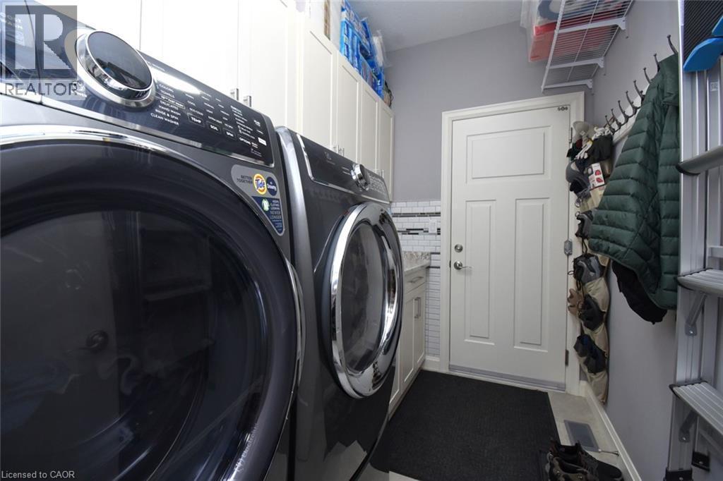 Dedicated laundry room featuring side-by-side washer and dryer units with modern black finishes, built-in wall shelving for storage, and direct access to the home's interior - 10 Craddock Boulevard, Jarvis, ON - Indoor Photo Showing Laundry Room